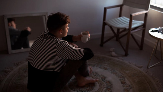 Teenage boy sitting on the floor in a room.